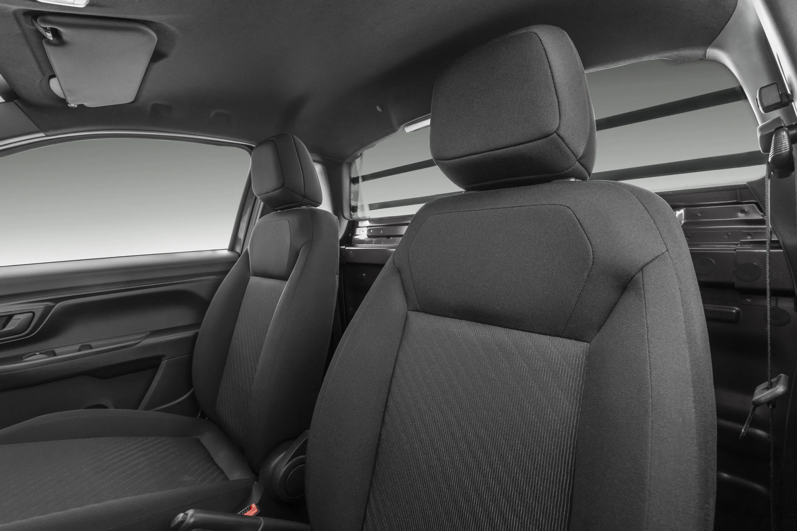 A cabine leva duas pessoas com conforto simples, ar-condicionado e espaço atrás dos bancos para ferramentas, mochilas e objetos de trabalho.